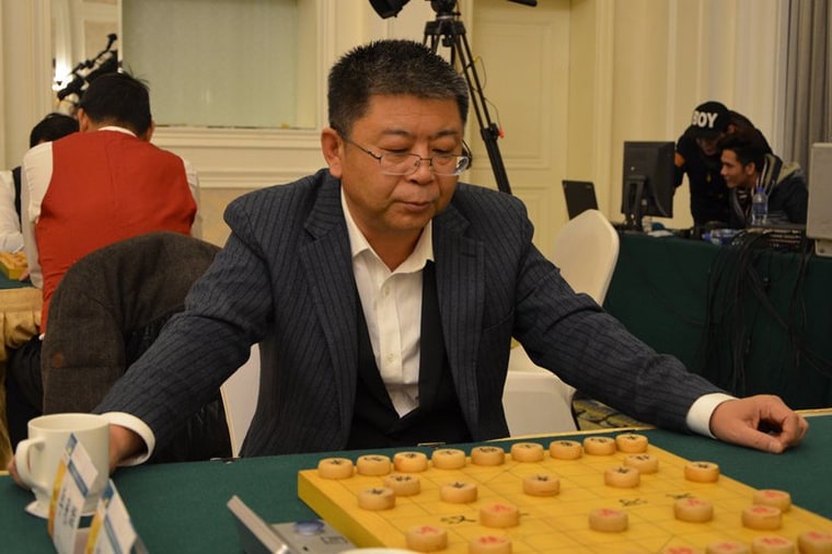 李来群身着条纹西装在棋盘前对局